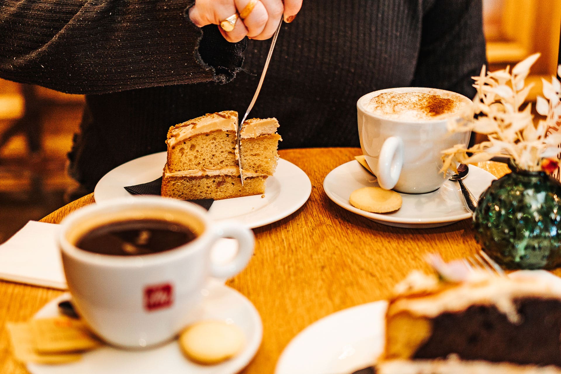 Woman cutting into a slice of cake with a cappuccino